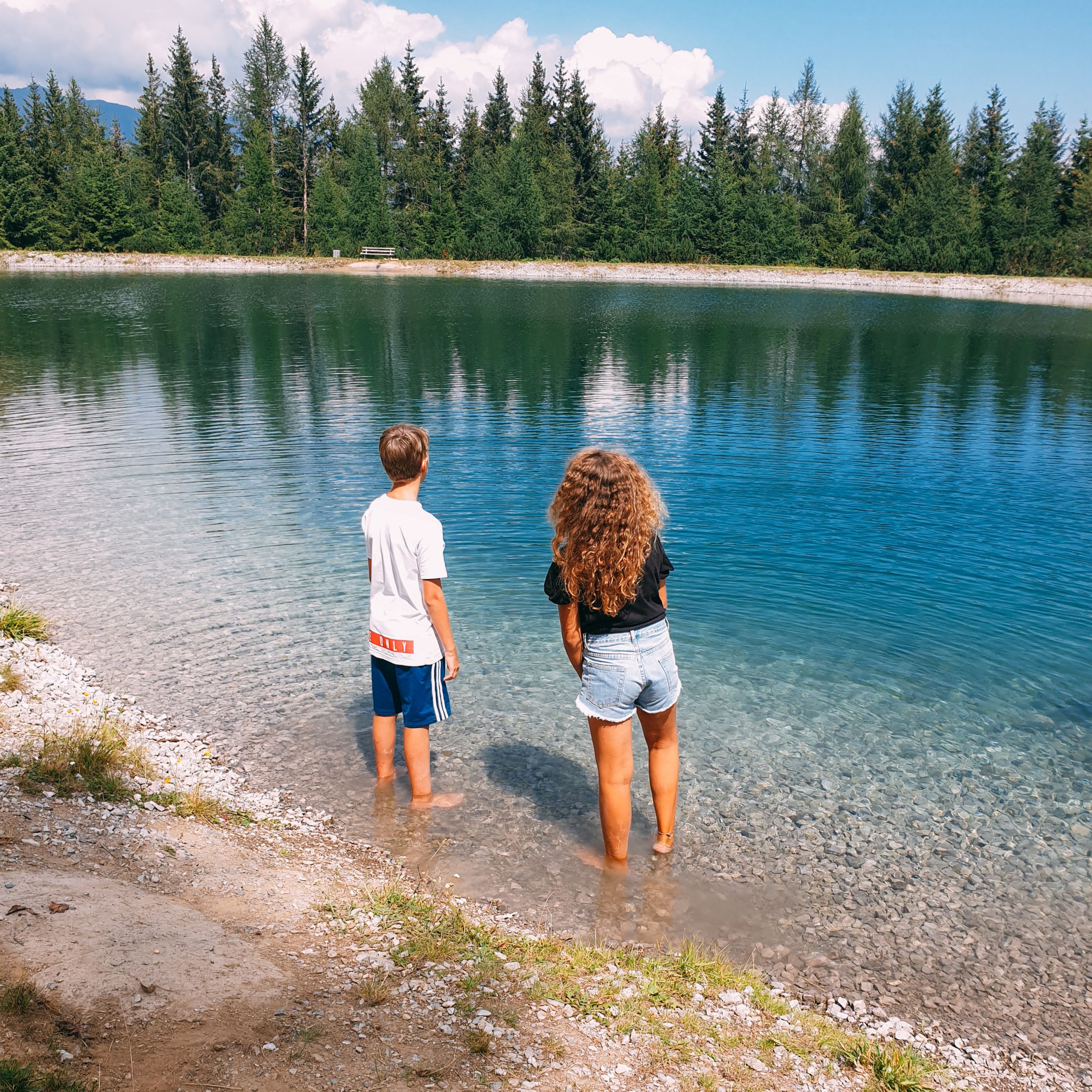 Due bambini in piedi sulla riva di un lago cristallino, vacanze all'aria aperta, viaggi organizzati per famiglie
